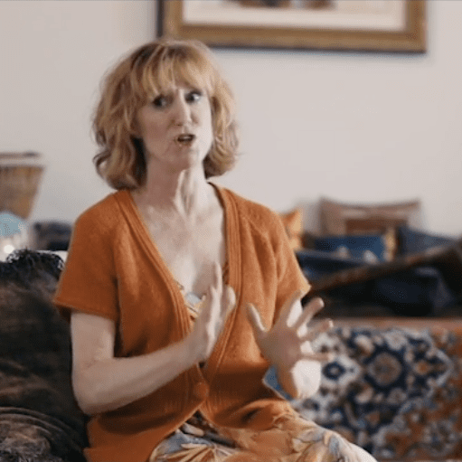 Woman in orange dress gesturing with hands indoors.